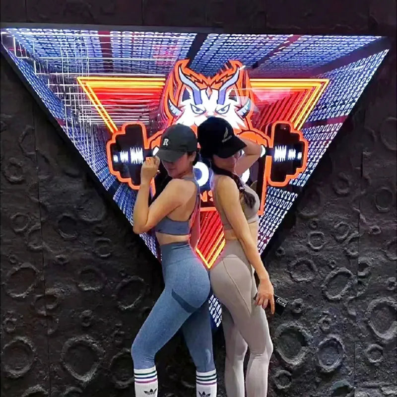 Two people beside a triangular gym infinity mirror