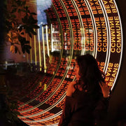 A woman stands by a Custom Logo Infinity Mirror, its endless lights reflecting a neon COMMUNE BEANS sign.