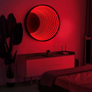 A bedroom featuring the Maytrix Circle Infinity Mirror with LED lights above a modern sideboard, a potted plant on the left, and a neatly made bed in front.