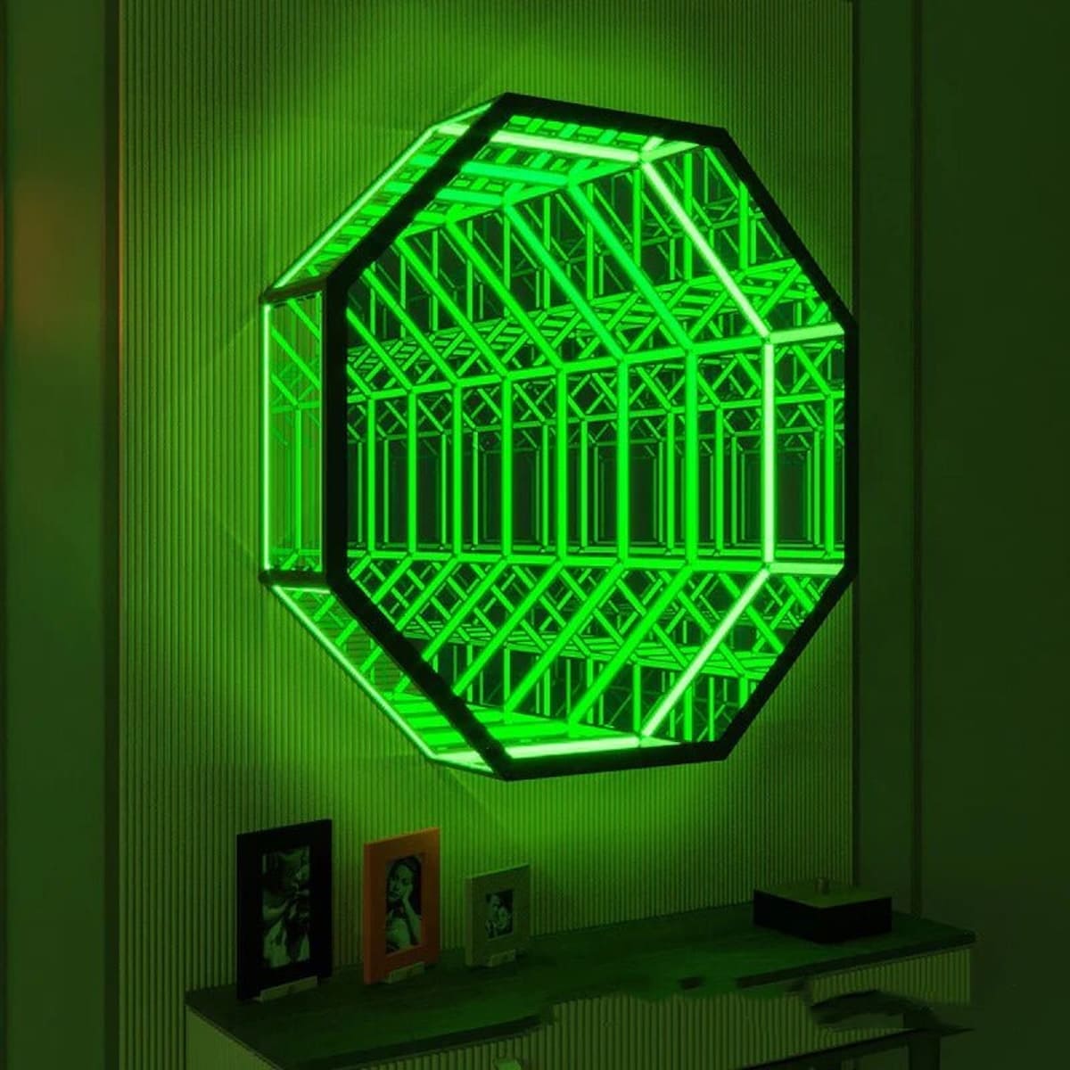 An Octagon Infinity Mirror with glowing green LED geometric patterns hangs above a shelf with framed photos.